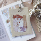 Notebook with floral design clipped to an open book, surrounded by dried flowers.