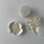 Cosmetic products including a jar, a white dish, and small containers on a light gray surface.
