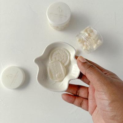 Hand holding a stamped Soft Glow wax seal with a pearly sheen, more seals arranged on a light backdrop