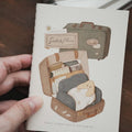 Notebook with illustration of a suitcase and teddy bear held by a hand