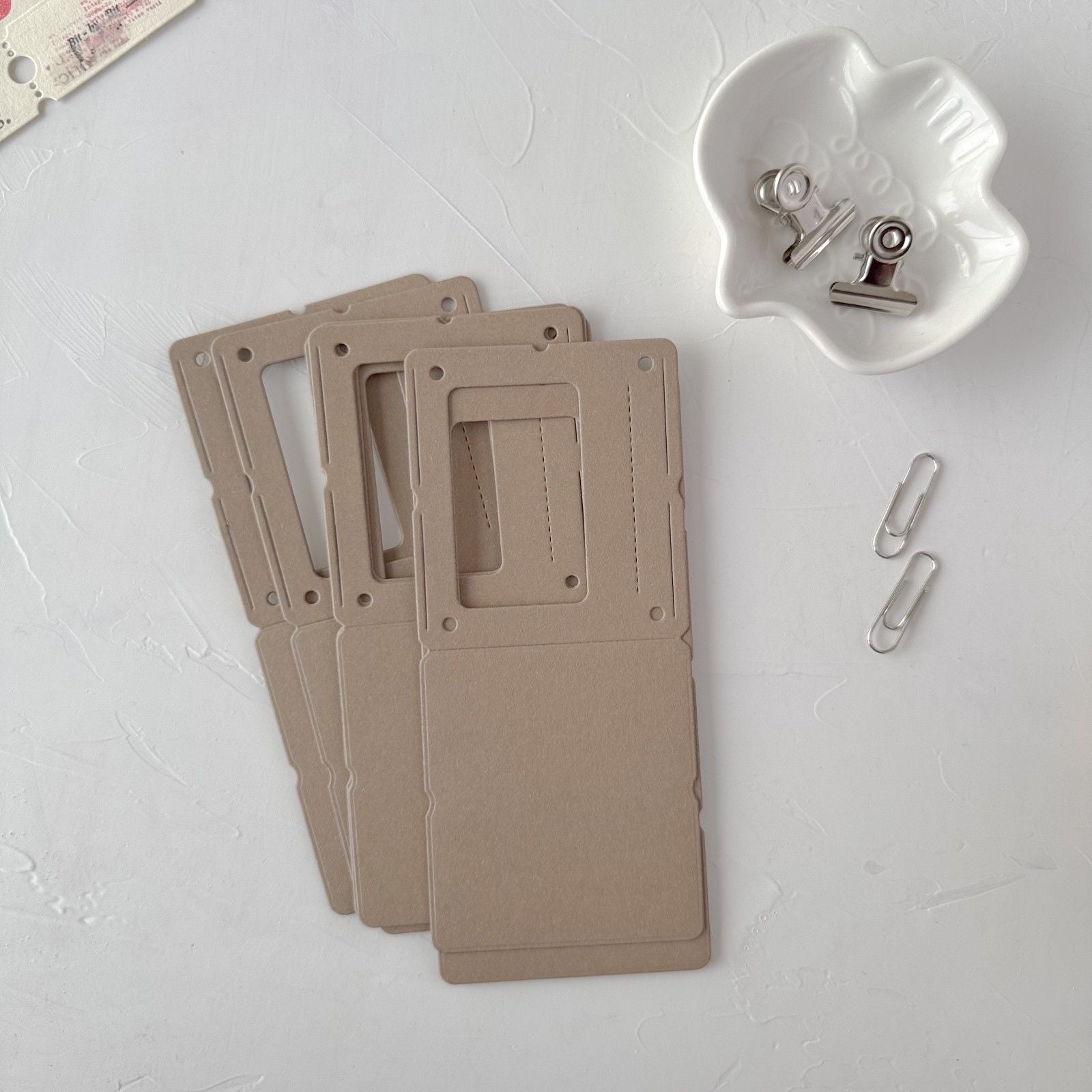 Three beige name tags with a paper clip on a light gray surface