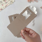 Hand holding a beige plastic card with cut-out shapes on a light gray background
