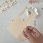 Hand holding a beige card with a clear plastic window on a light gray background