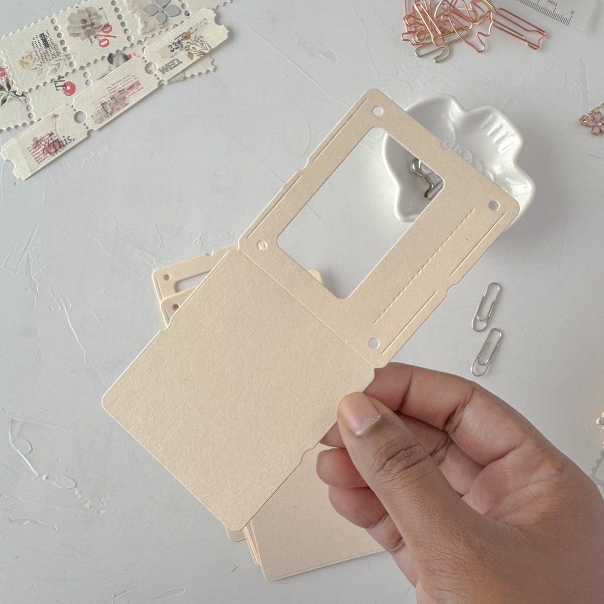 Hand holding a cream Specimen Card Vol. 1 card with a window cutout on light grey