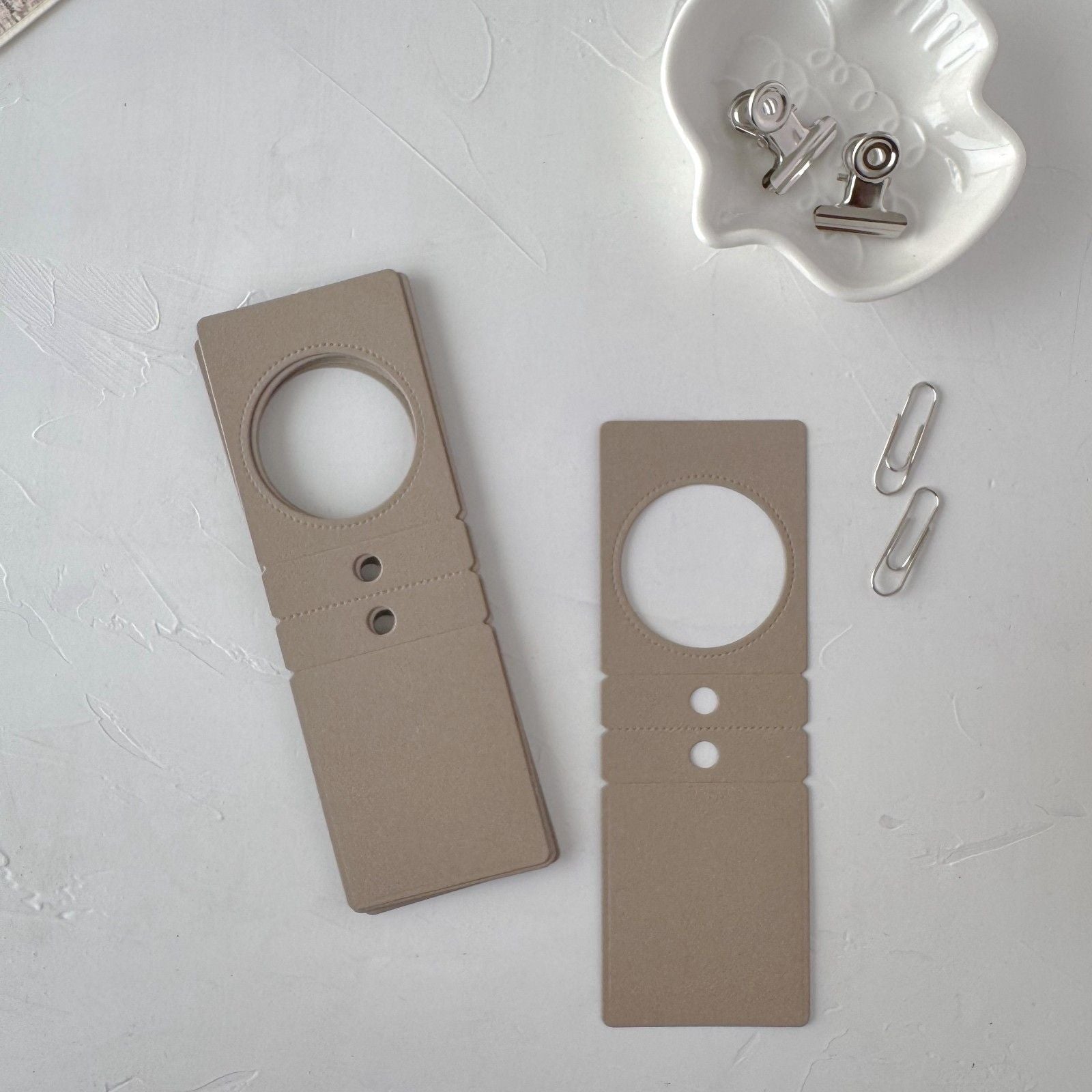 Two beige door hangers on a light gray surface with paper clips.