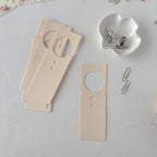 Wooden door hangers on a light gray surface with a white ceramic holder and paper clips.
