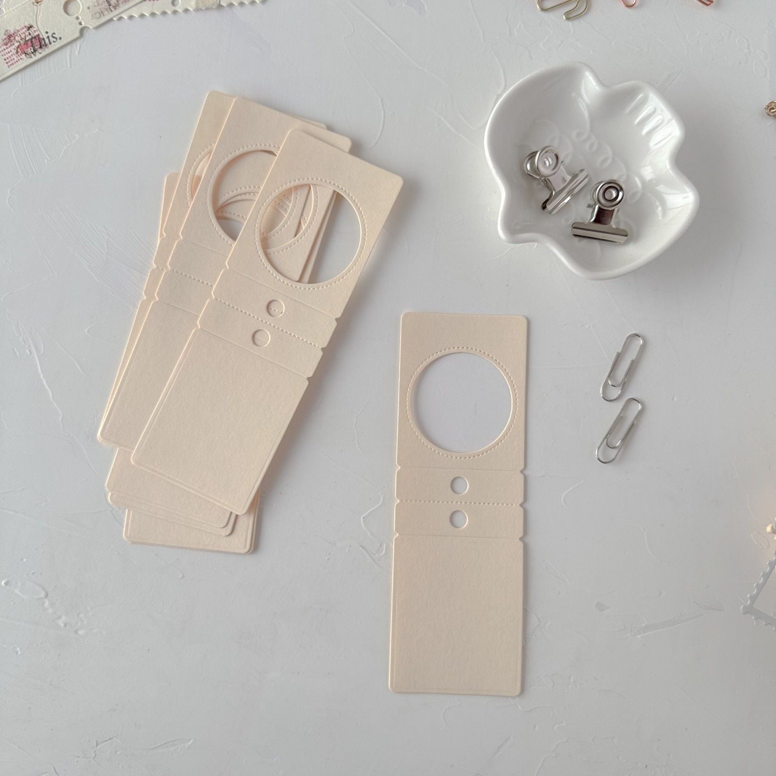 Wooden door hangers on a light gray surface with a white ceramic holder and paper clips.
