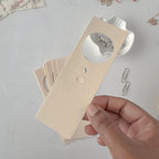 Hand holding a beige card with cut-out shapes on a light gray surface