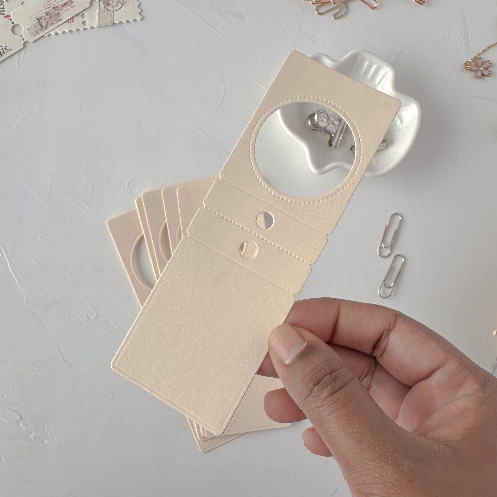 Hand holding a beige card with cut-out shapes on a light gray surface