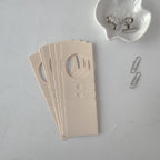 Beige cardboard product with cut-out design on a gray surface, accompanied by small clips.