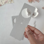 Hand holding a small metal tool on a light gray surface with paper clips.