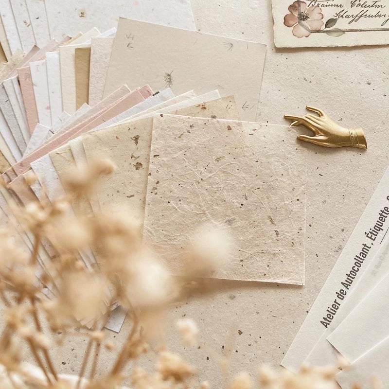 Collection of beige textured papers with a decorative gold hand and dried flowers on a light surface.