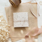 Small wrapped gift on top of vintage-looking paper with ribbons and flowers.