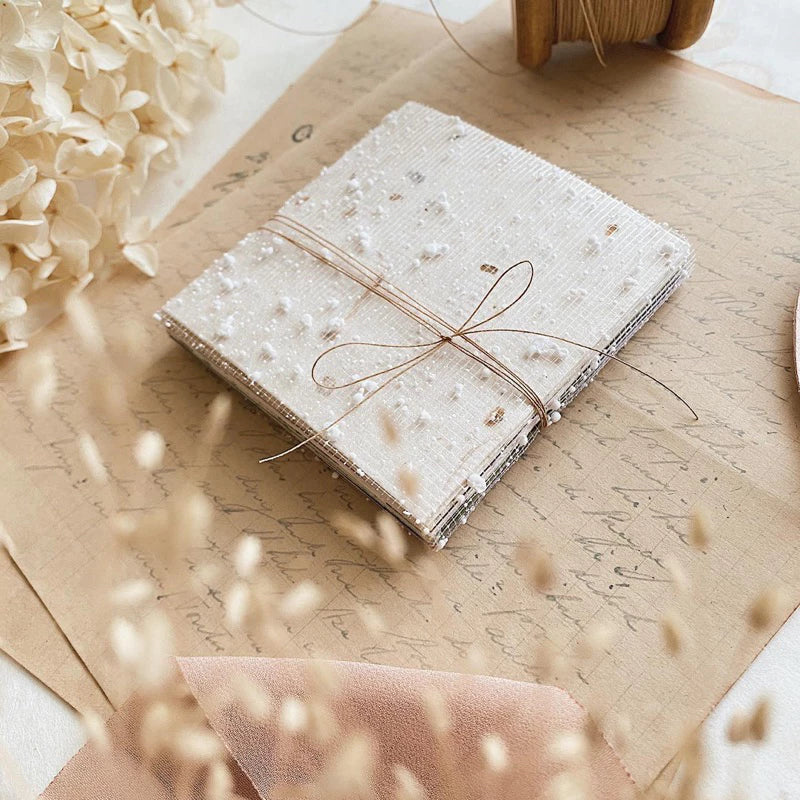 White textured Square Paper Vol. 2 sheets tied with brown string on a wooden surface