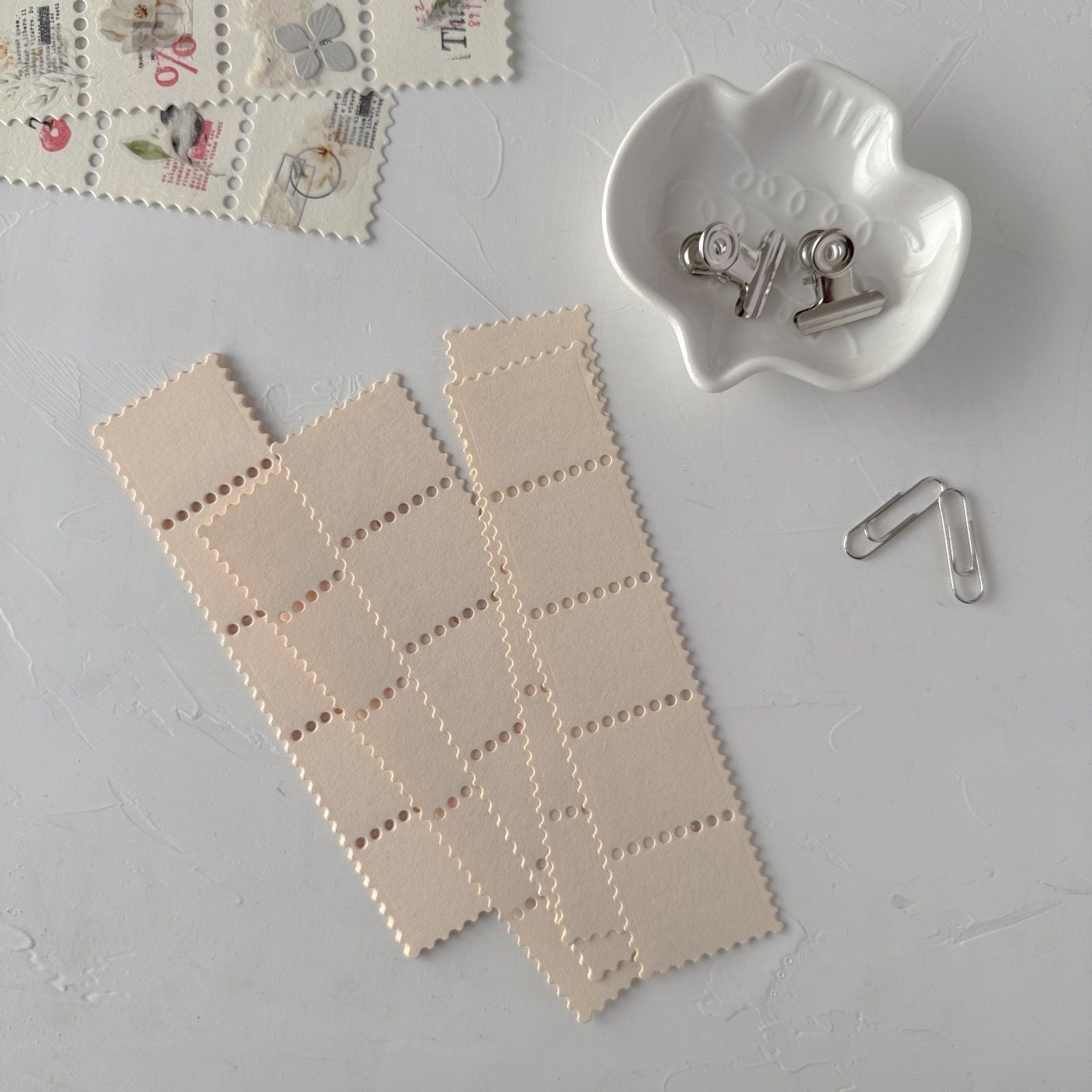 Two cream Stamp Card Vol. 1 strips with a small white dish of metal clips on light grey