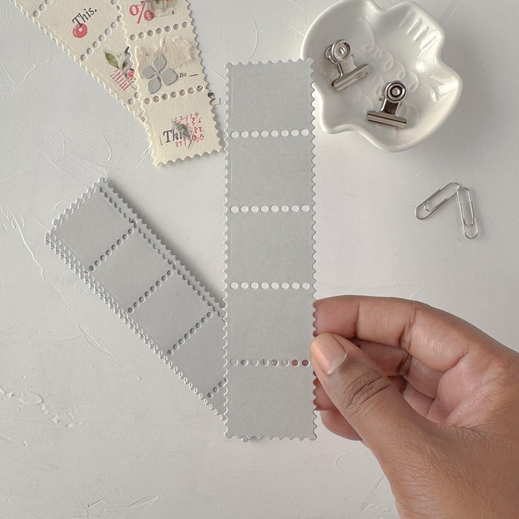 Gray fabric swatch with a hand holding it, surrounded by decorative stamps and clips on a light gray background.