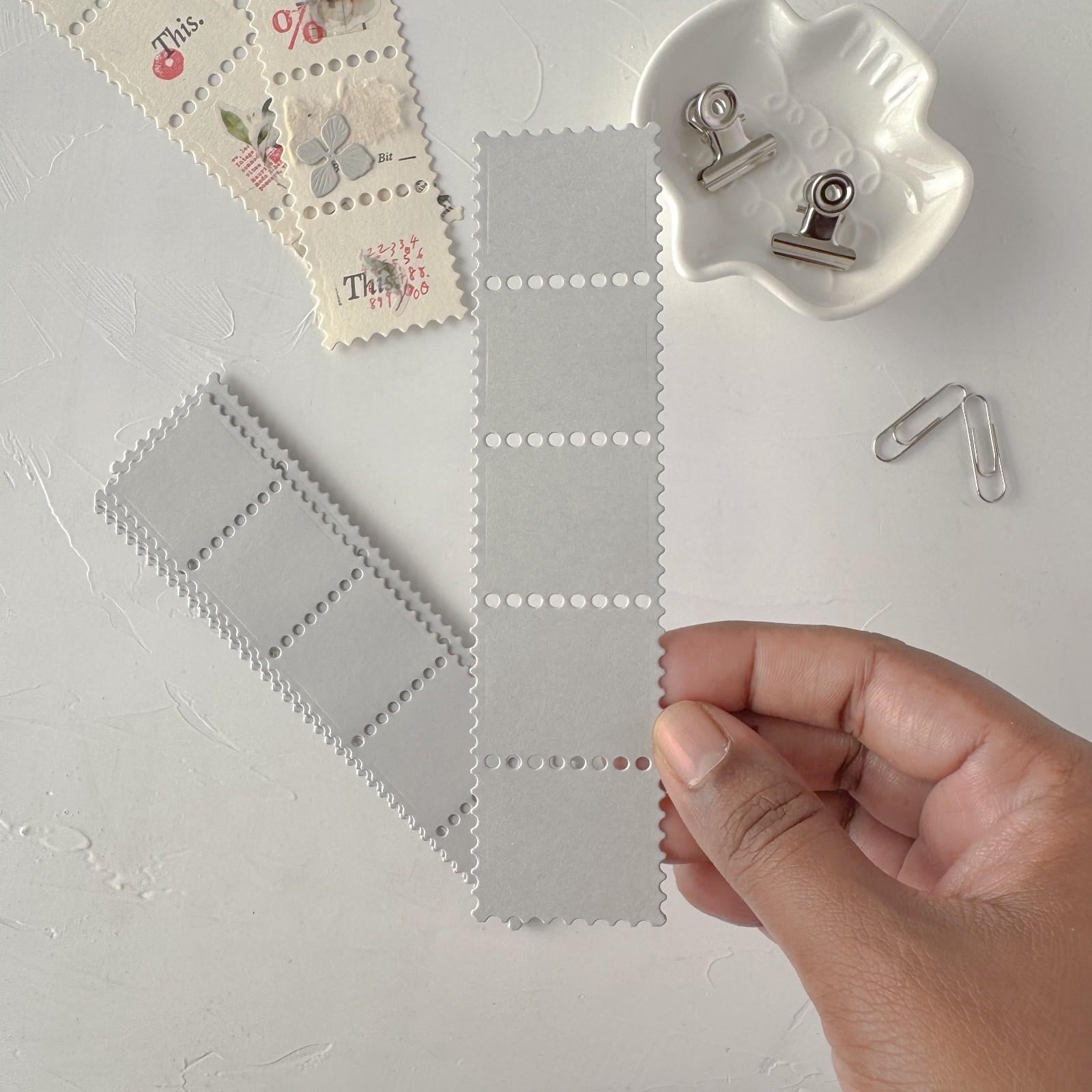 Hand holding a grey Stamp Card Vol. 1 ephemera card with stamps and clips styled on light grey