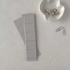 Gray paper clips on a light gray surface with a small white dish and metal clip.