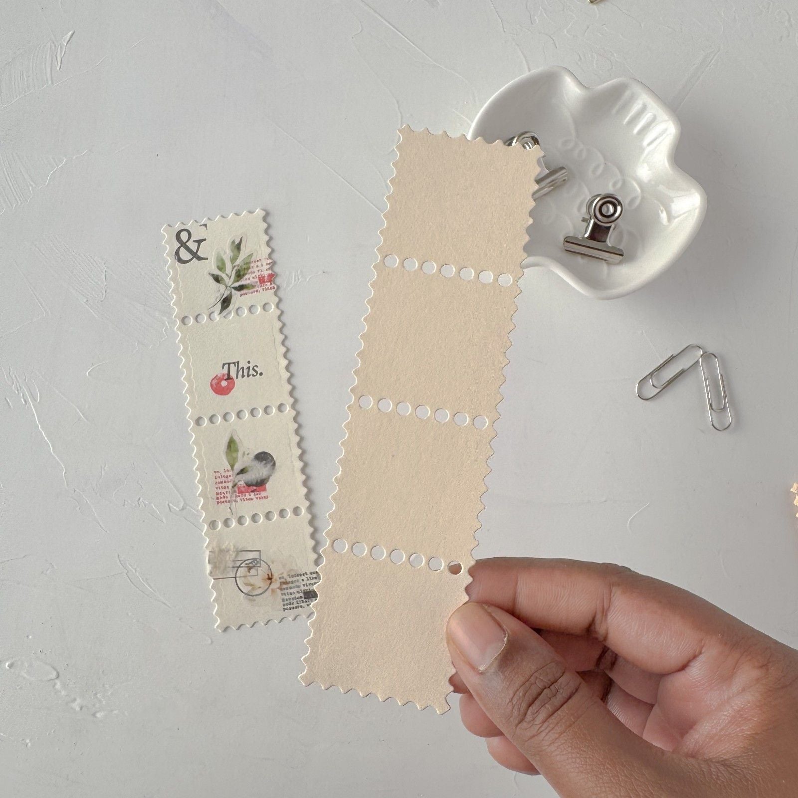 Hand holding a piece of beige fabric with printed designs on a light gray background