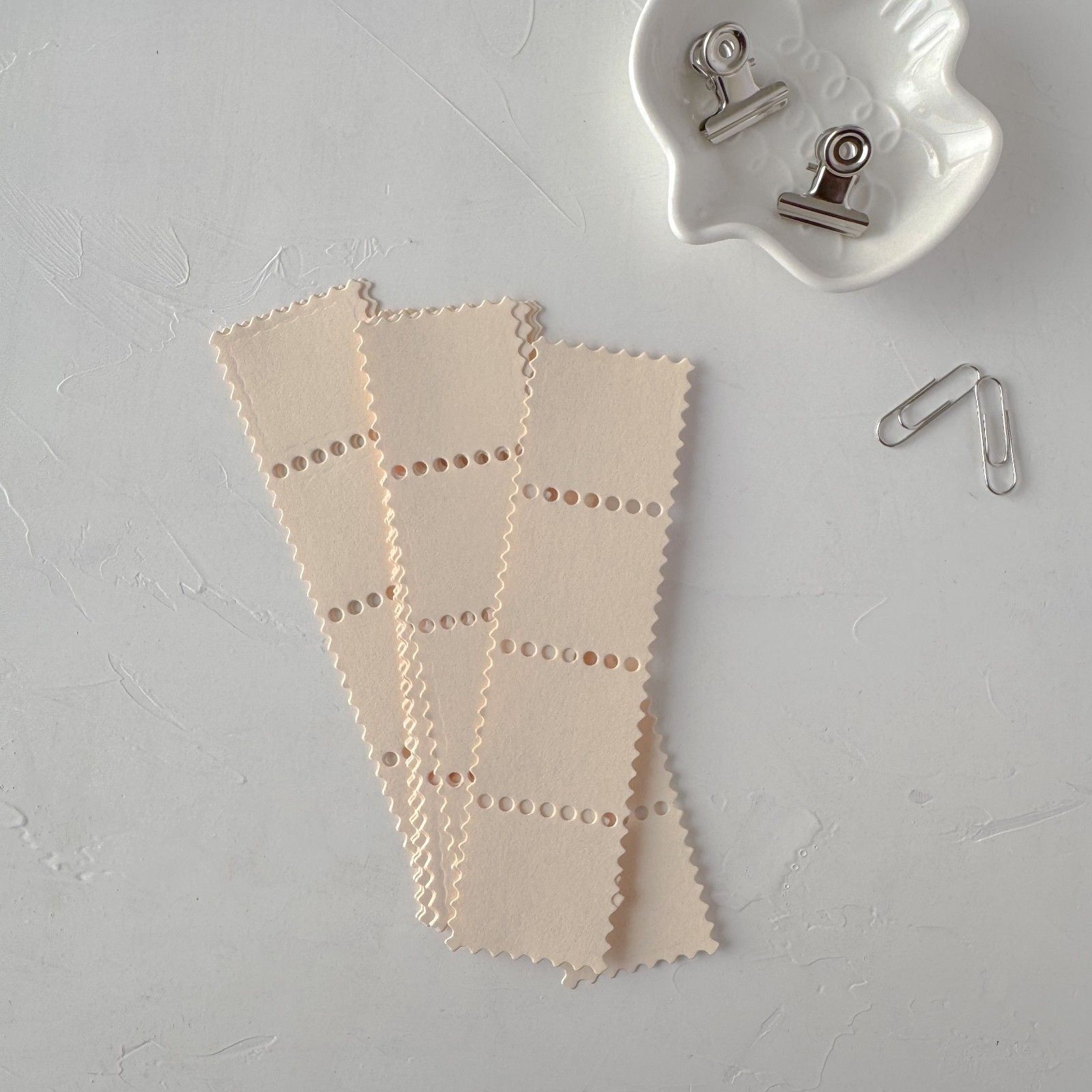 Beige paper clips on a light gray surface with a white container.