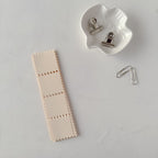 Beige leather strip with stitching, white ceramic holder with clips, and additional metal clips on a light gray background.