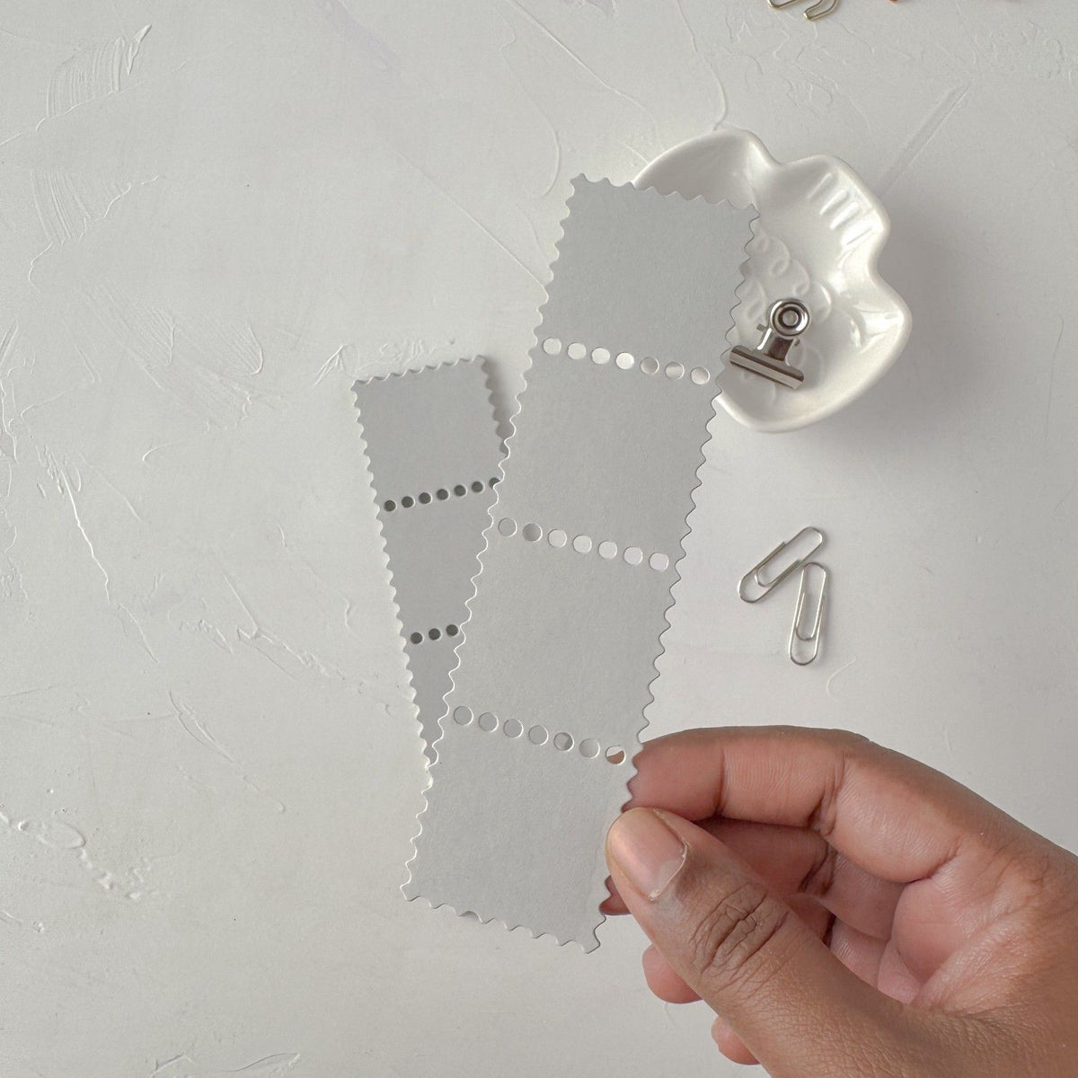 Hand holding a grey Stamp Card Vol. 2 card with a clip on a textured white background