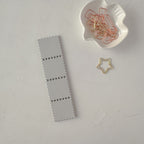 Gray bookmark with perforated design on a light gray surface with decorative paper clips.