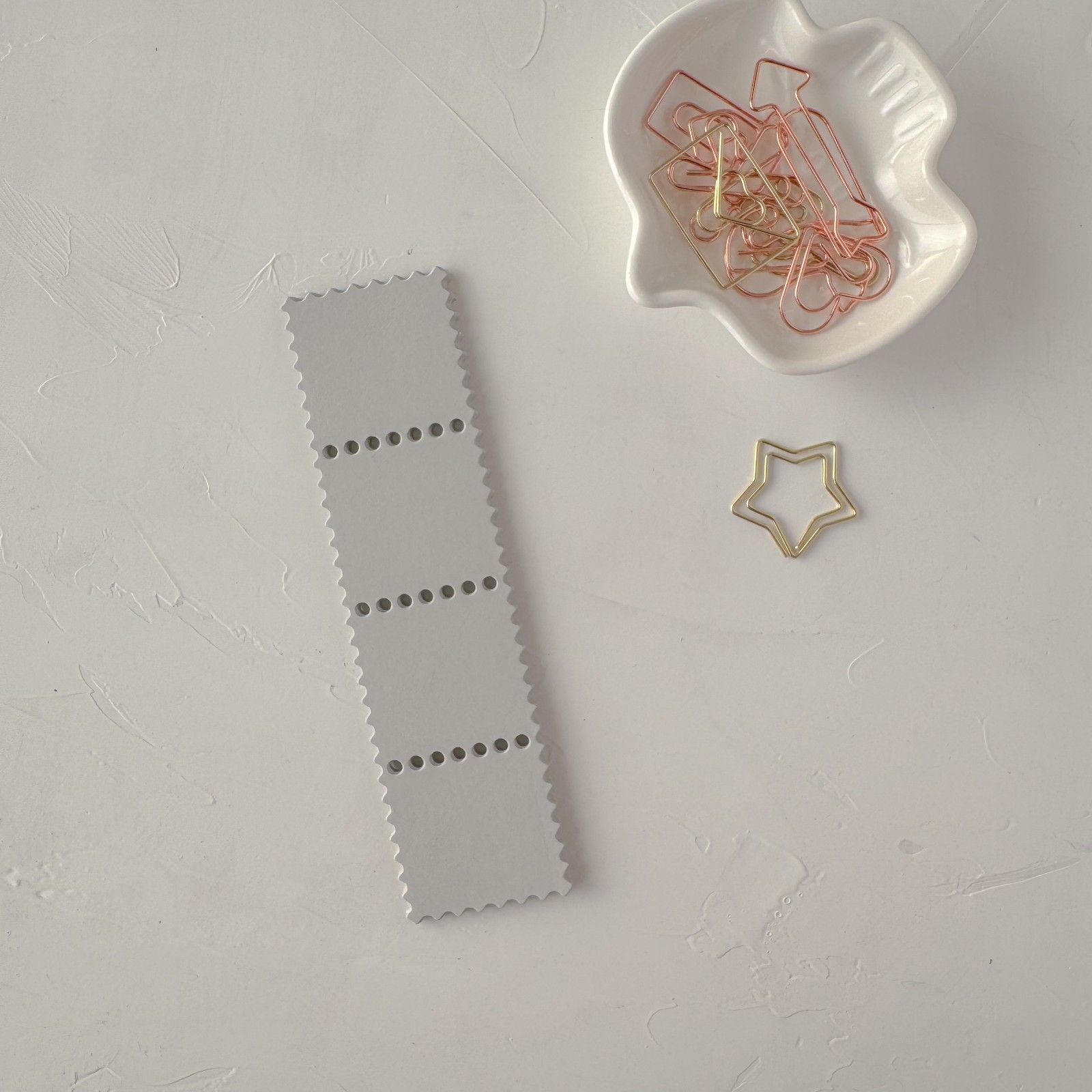 Gray bookmark with perforated design on a light gray surface with decorative paper clips.