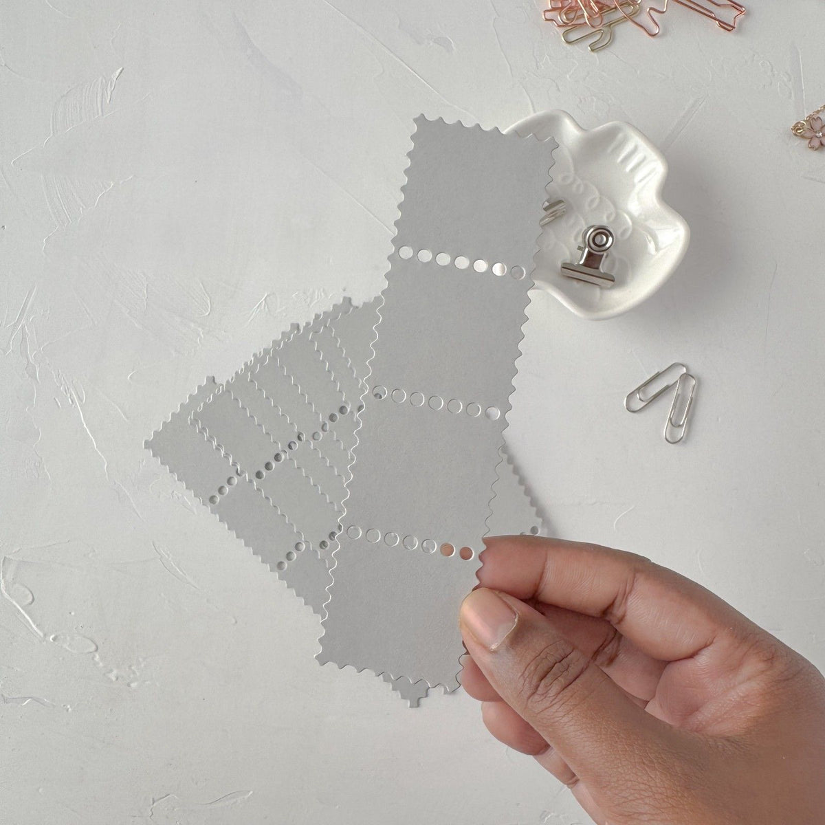 Hand holding a grey Stamp Card Vol. 2 card with decorative paper clips on light grey
