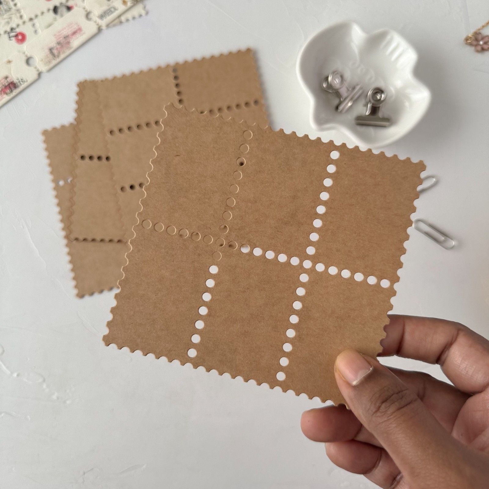 Brown paper with cut-out patterns held by a hand on a white surface.