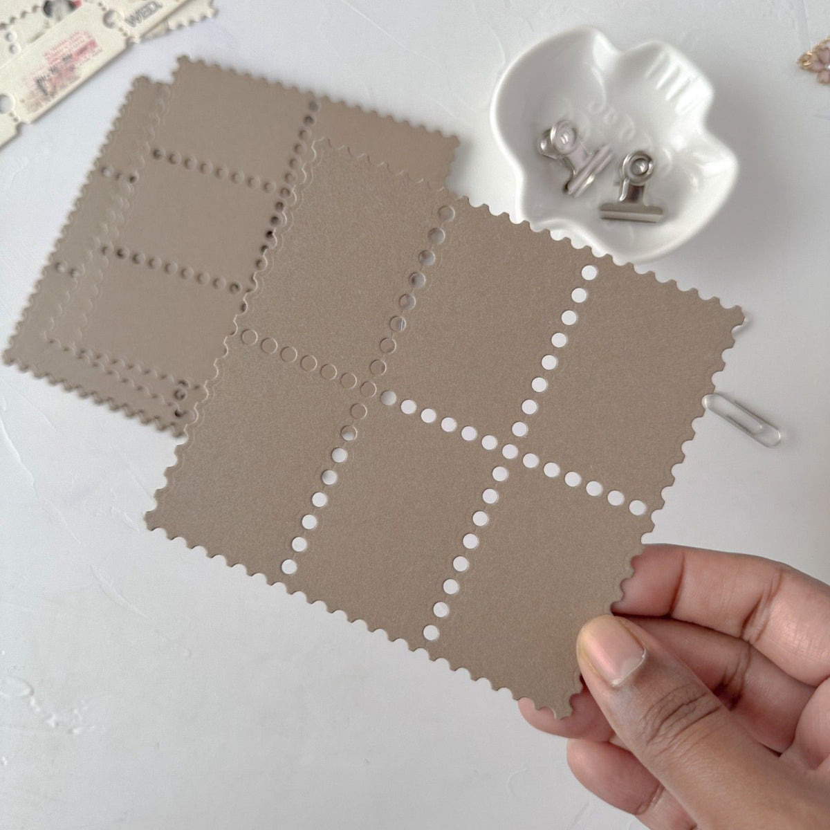 Hand holding a coffee-toned Stamp Card Vol. 3 card with a grid pattern on a white backdrop