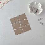 Brown square patch with white dots on a light gray surface with a white clip and paper clips.