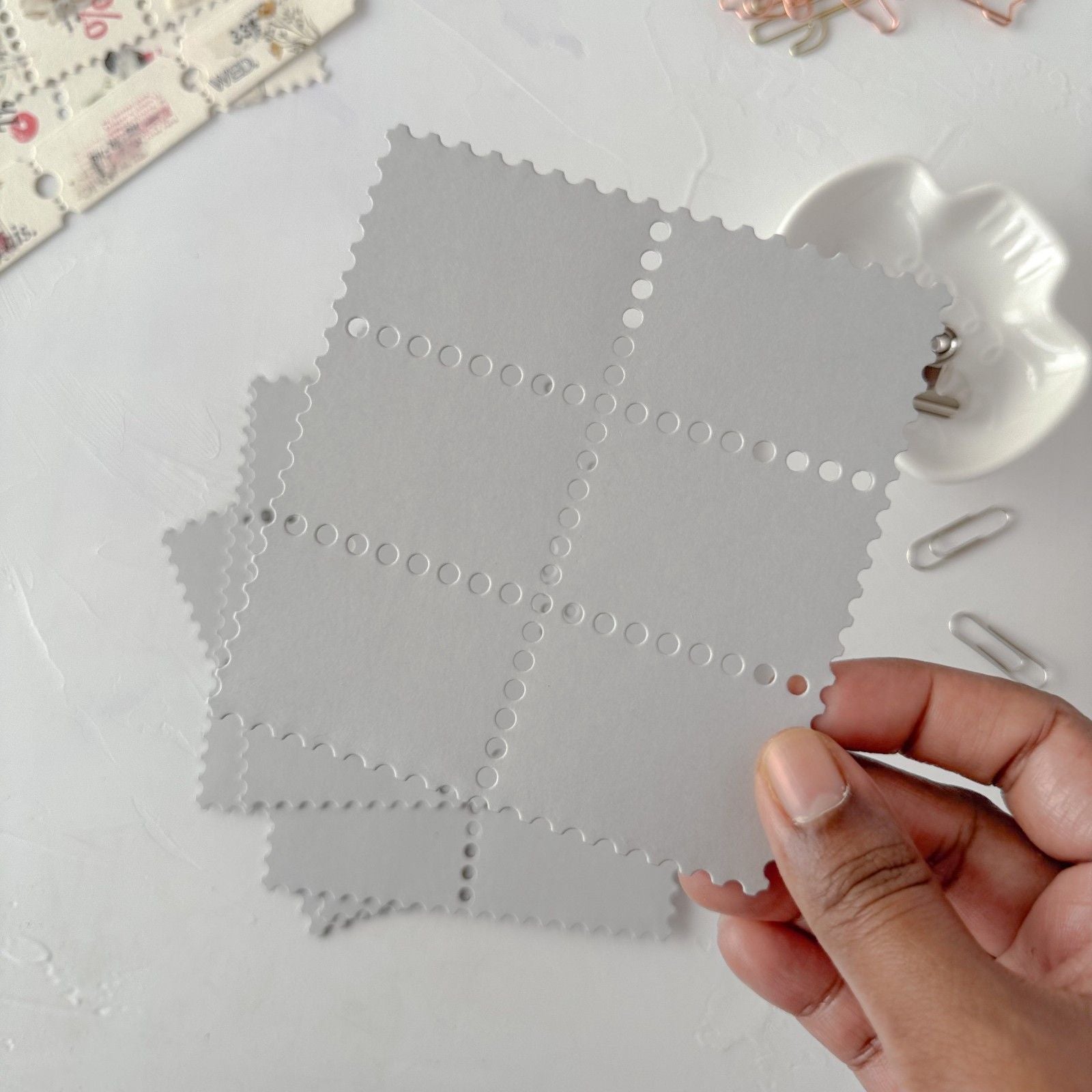Hand holding a gray fabric swatch with circular cutouts on a light surface.