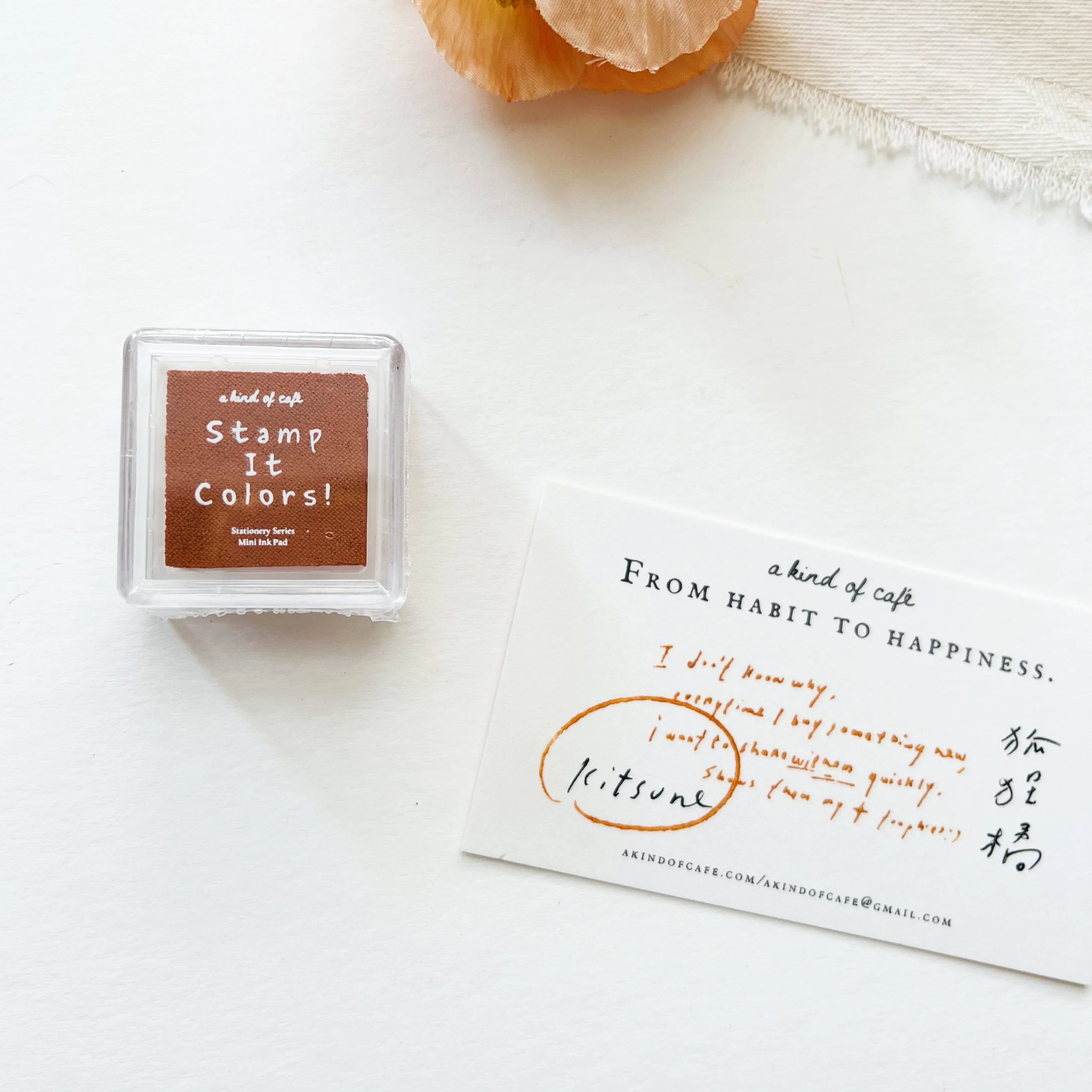 Square stamp with 'Stamp It Colors!' text on a white surface with a piece of paper and orange fruit.