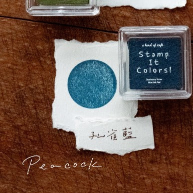 Blue ink stamp on white paper with 'Stamp It Colors!' container on a wooden surface