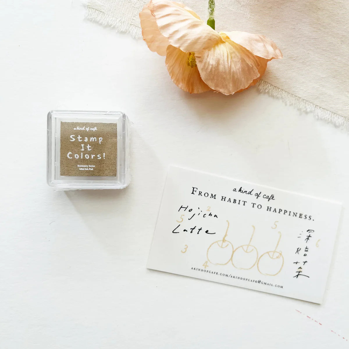 Small square stamp pad with 'Stamp It! Colors!' text, a card with text and illustrations, and a peach-colored flower on a white background.