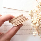 Hand holding wooden blocks with engraved text on a white surface with flowers.