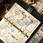 Planner with decorative stickers and a gold ring binder on a wooden surface.