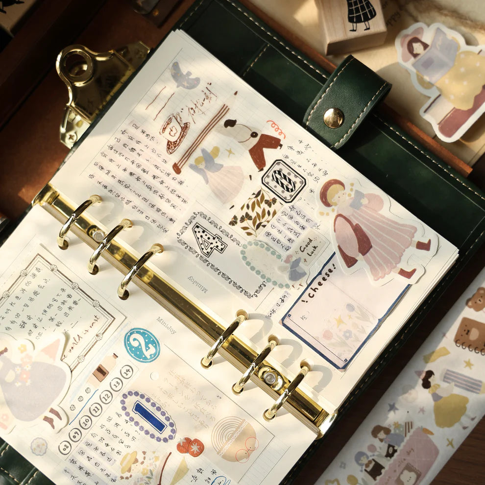 Gold ring-bound planner decorated with Stationery Planet PET Tape stickers on a wooden desk
