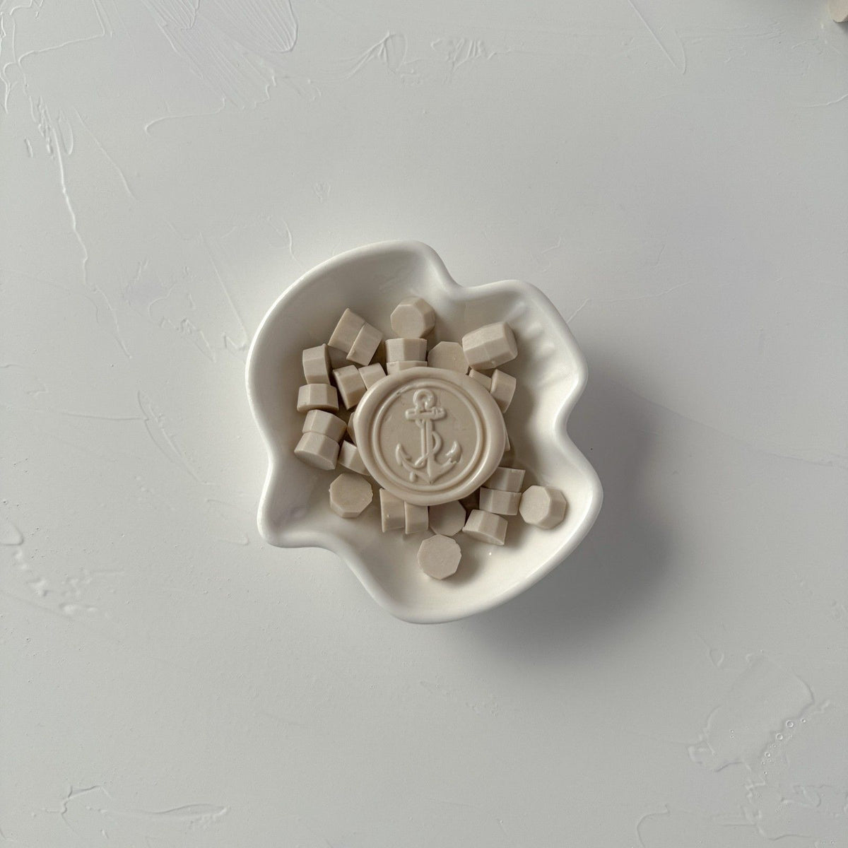 Small white dish of Steamed Milk sealing wax beads in a soft off-white tone, minimal flat lay on light grey