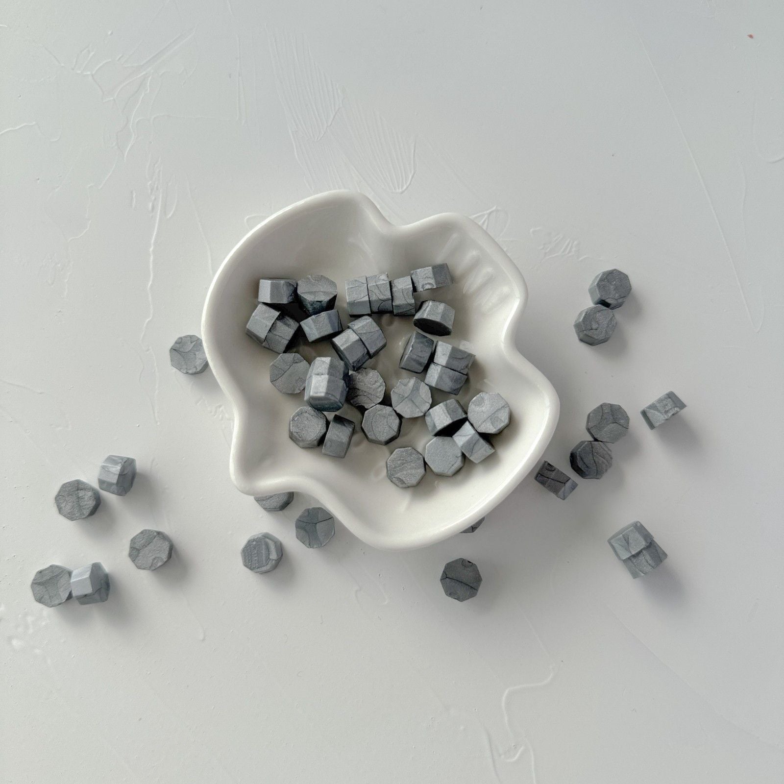 White dish filled with small gray hexagonal objects on a light gray background