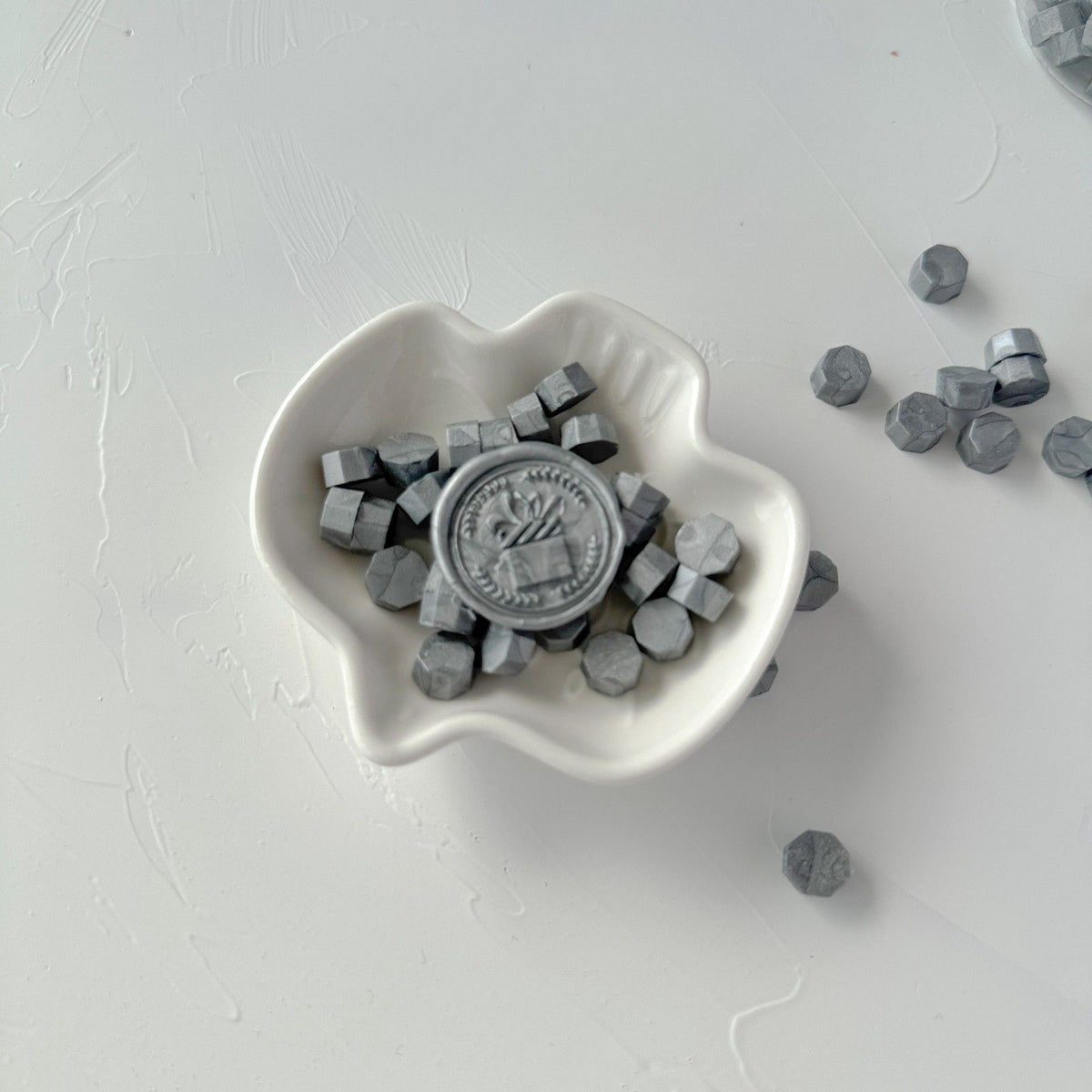 Heart-shaped white dish of cool-toned Steel Grey Wax Beads styled on a soft light grey background
