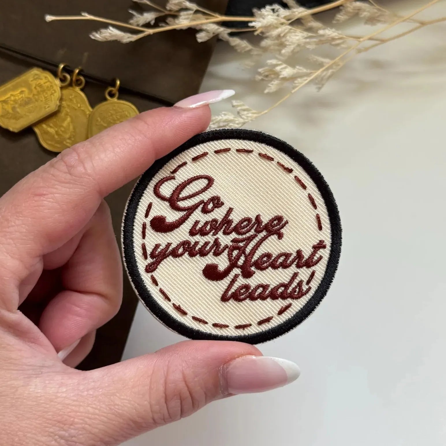Hand holding a patch with 'Go where your heart leads' text against a neutral background