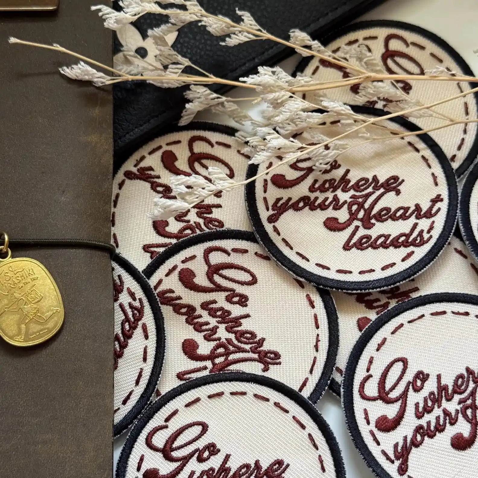Embroidered patches with motivational text on a textured surface with a gold coin and dried flowers.