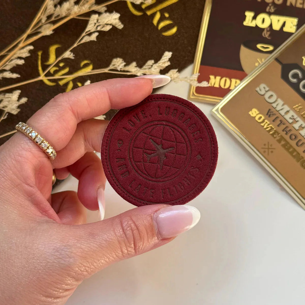 Hand holding a red circular object with embossed text and design, against a background with decorative elements.