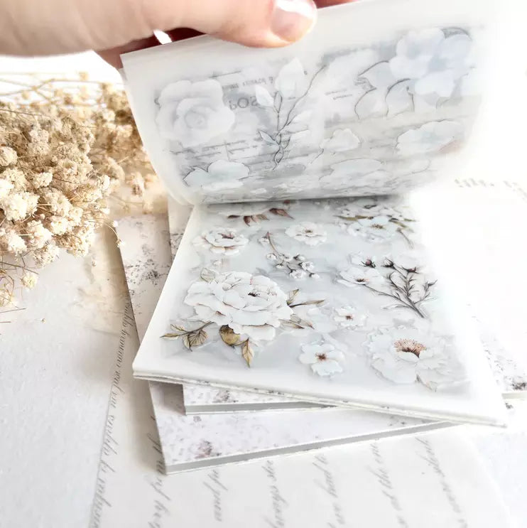 Hand lifting a floral page from The Vintage One Sticker Book stack on a light background