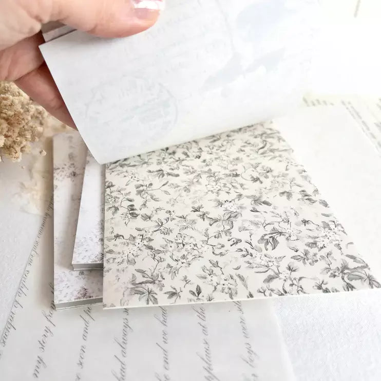 Hand holding a stack of The Vintage One Sticker Book floral pages on a textured surface