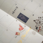 Planner calendar page decorated with a small piece of dark blue washi tape showing a character under stars, alongside festive doodles and handwritten notes.
