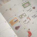 Planner calendar page decorated with colorful mood stickers, handwritten notes, and small festive icons like a candy cane and stocking.
