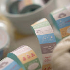 Close-up of pastel mood-tracking washi tape rolls with small icons, stars, and labels like “happiness level” and “happy day.